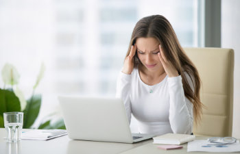 annoyed tired woman at desk in front of laptop at work